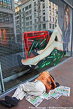 A homeless man sleeps in front of a photo of a glamorous model, San Francisco, California.